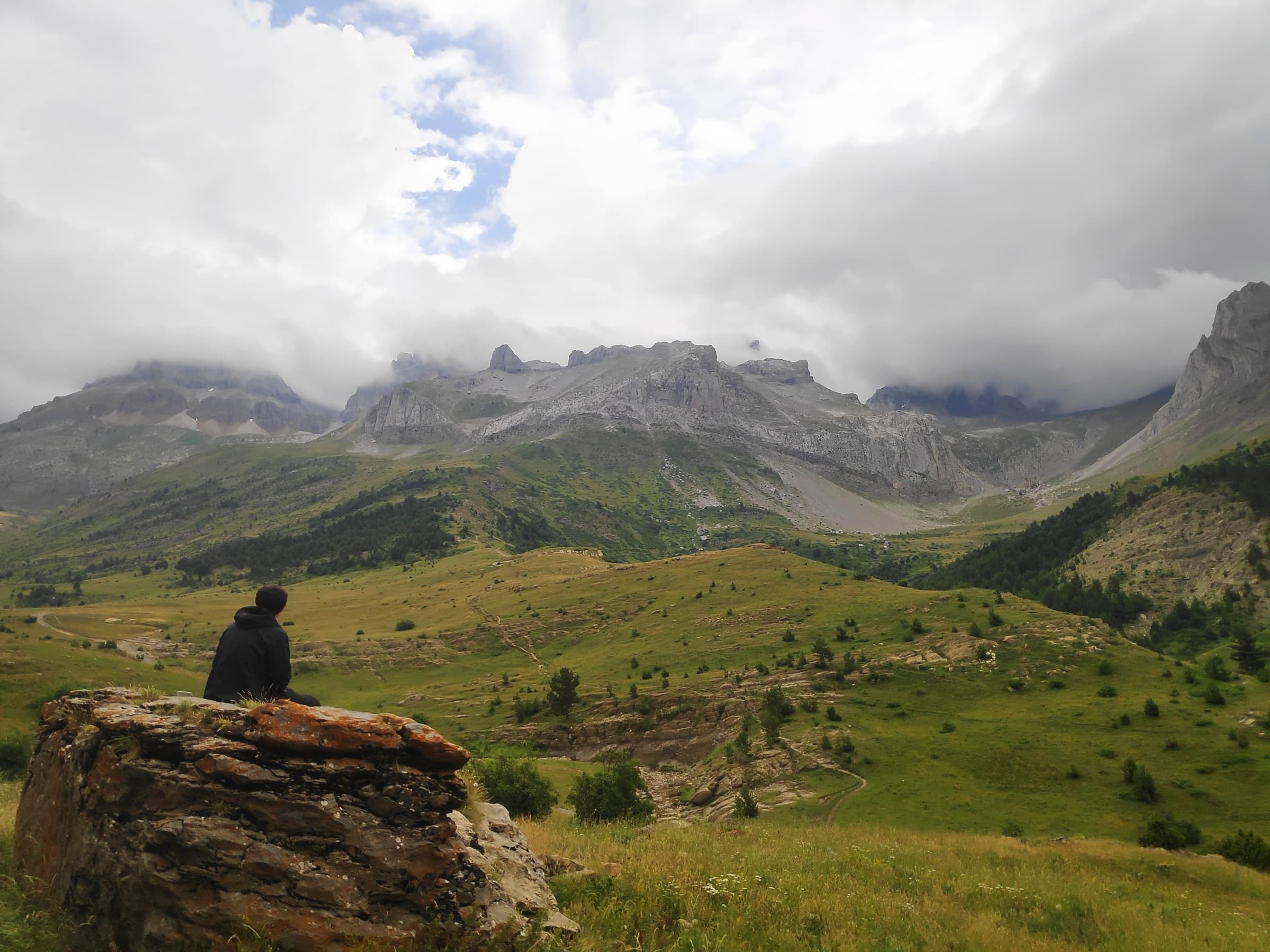 A hiker sitting on a rock outcrop above a green valley