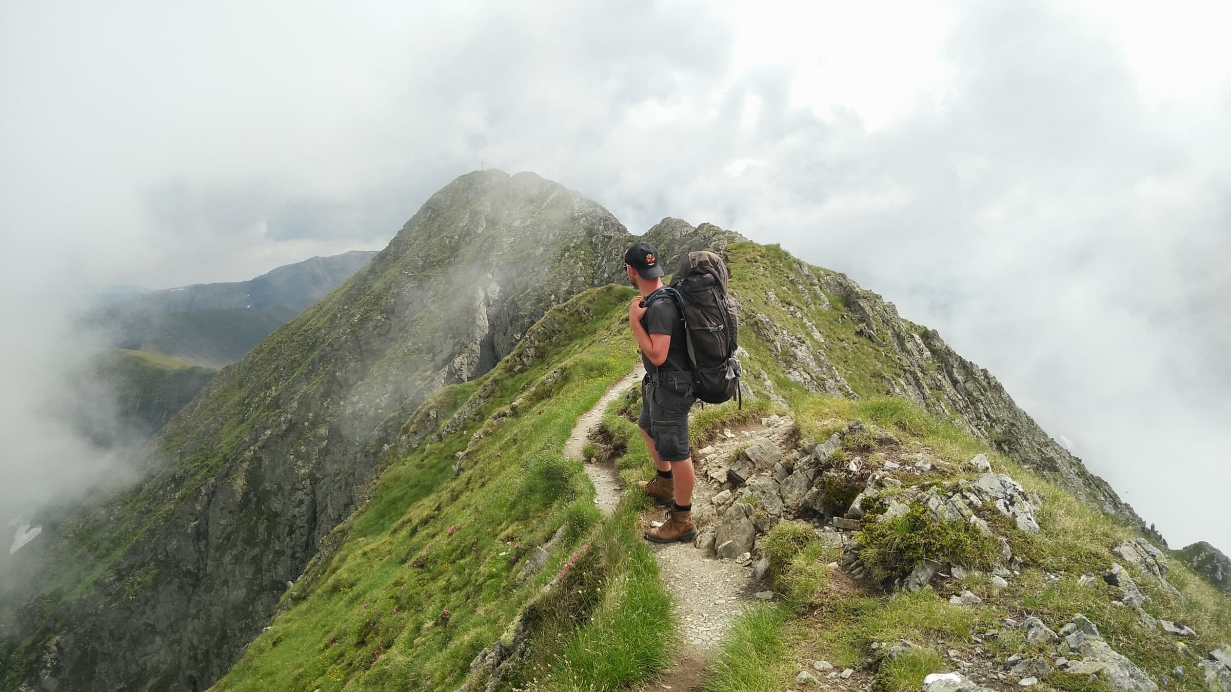 A backpacker walking a grassy ridge line into thick cloud