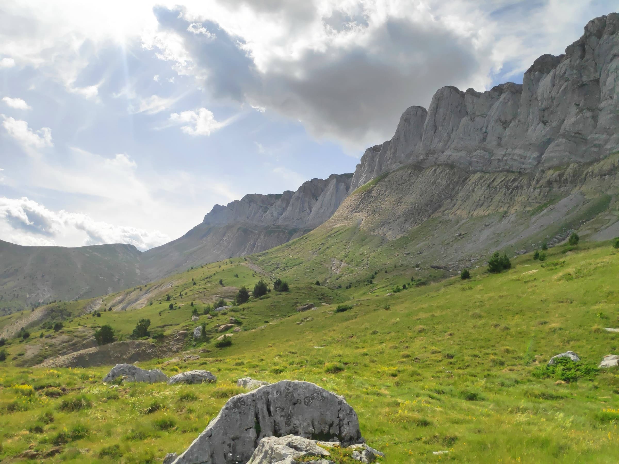 Pale limestone cliffs rising above steep green meadows