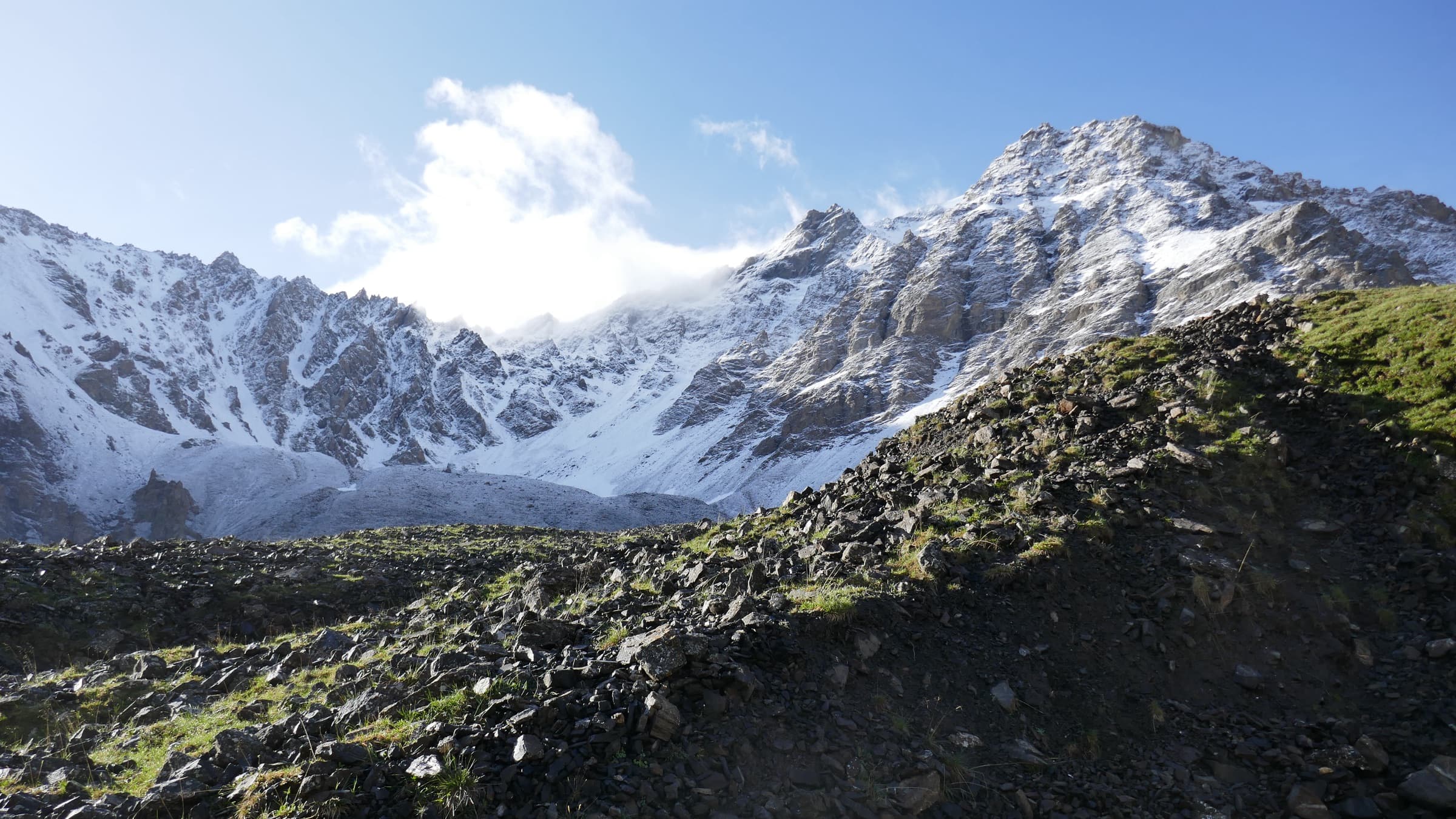 A snow-dusted peak above green slopes under a blue sky