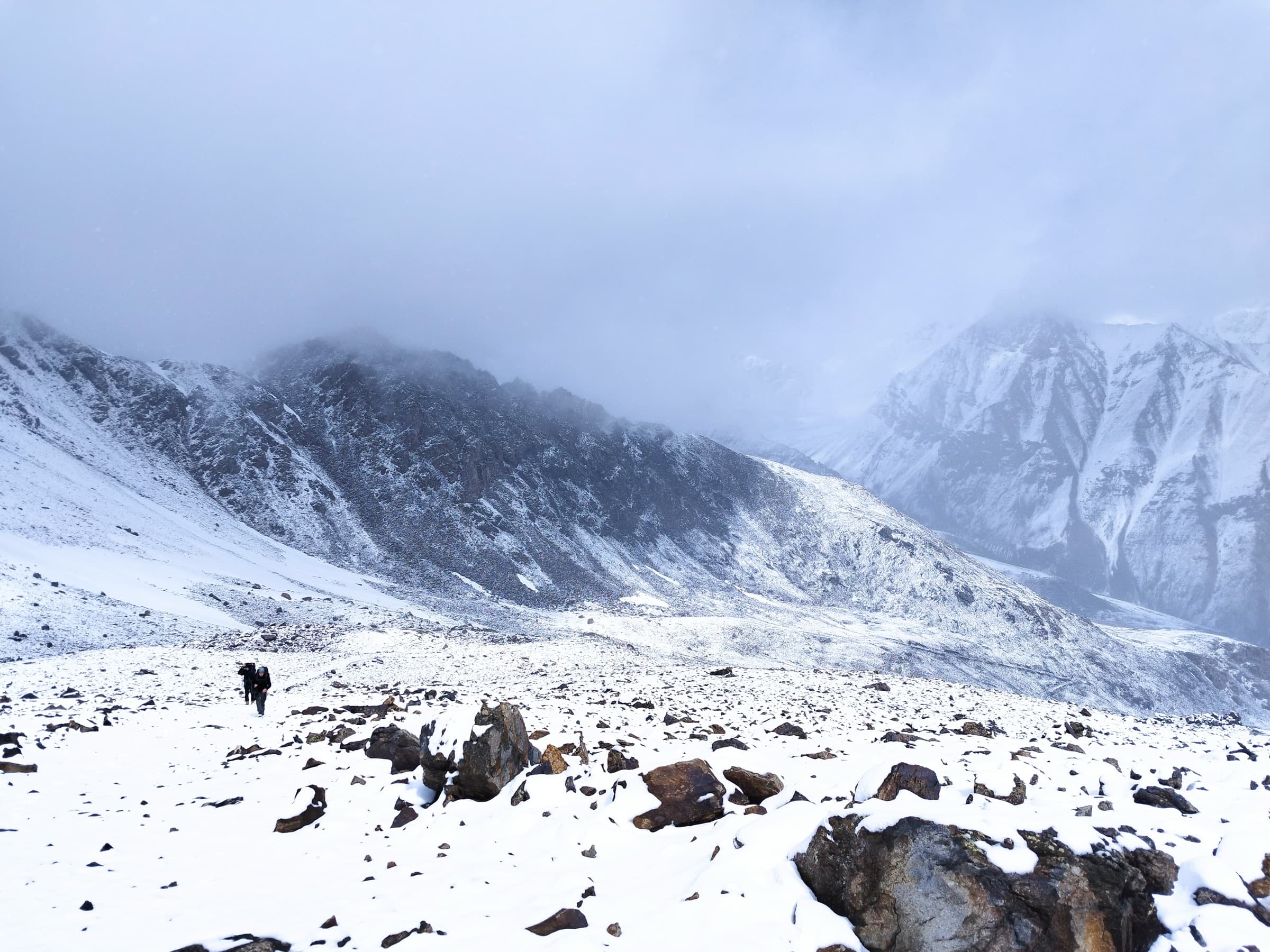 A hiker crossing a boulder field under fresh snow and low cloud