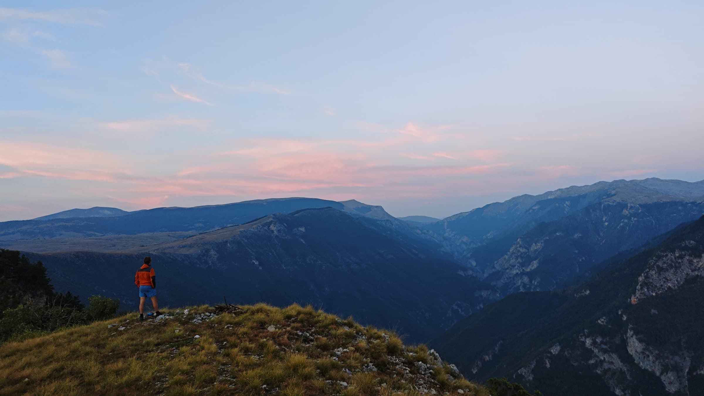 A pink and violet dusk sky over darkening ridges, watched from a high viewpoint