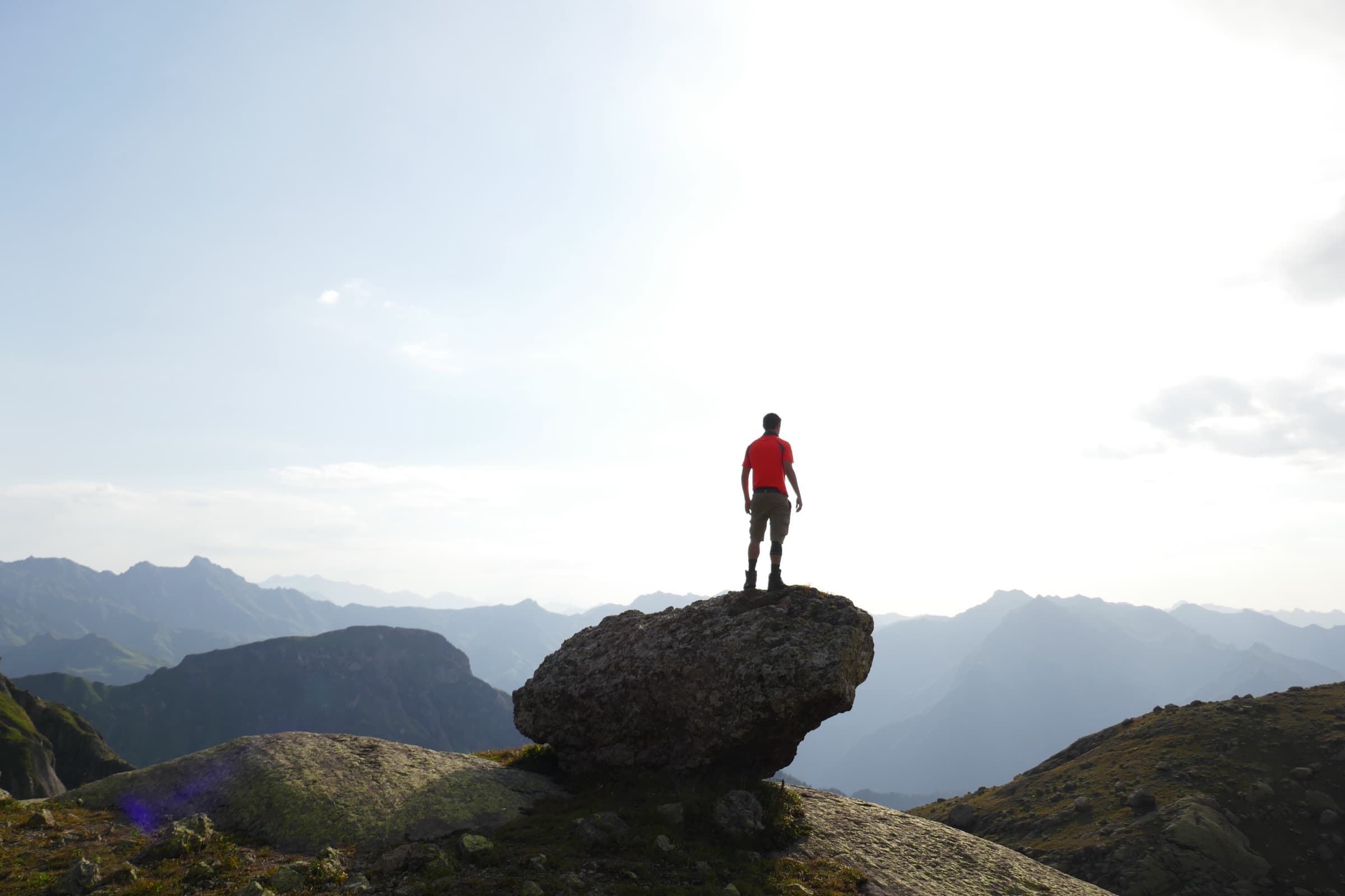 A hiker standing on a huge boulder against bright morning backlight, ridges fading into haze