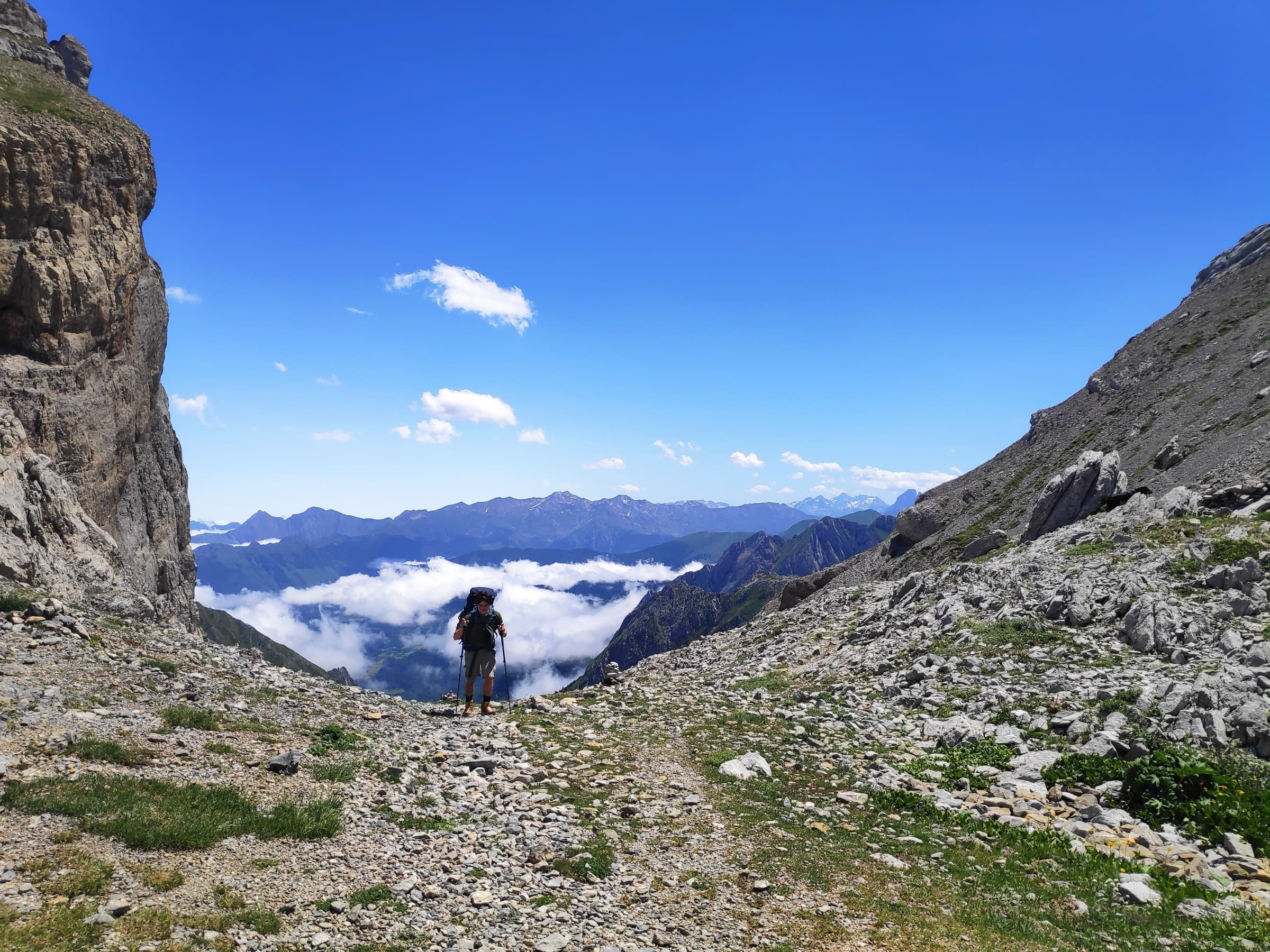 A hiker descending a stony path towards a gap filled with cloud