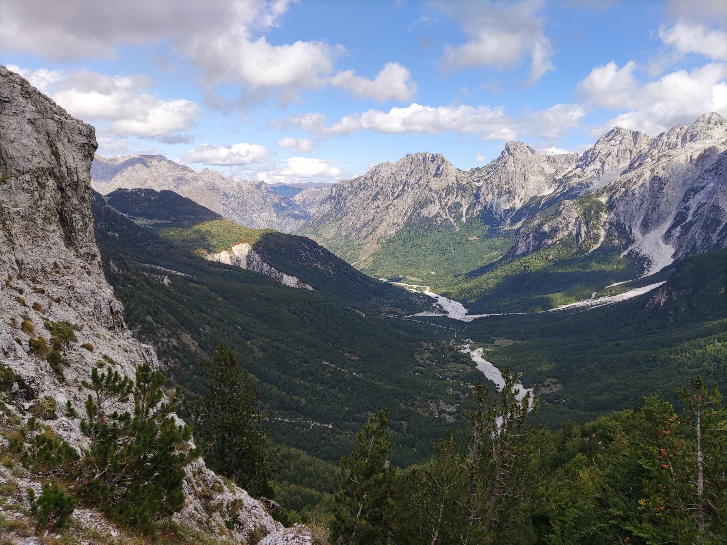 A deep green valley flanked by limestone peaks, with a riverbed winding through it