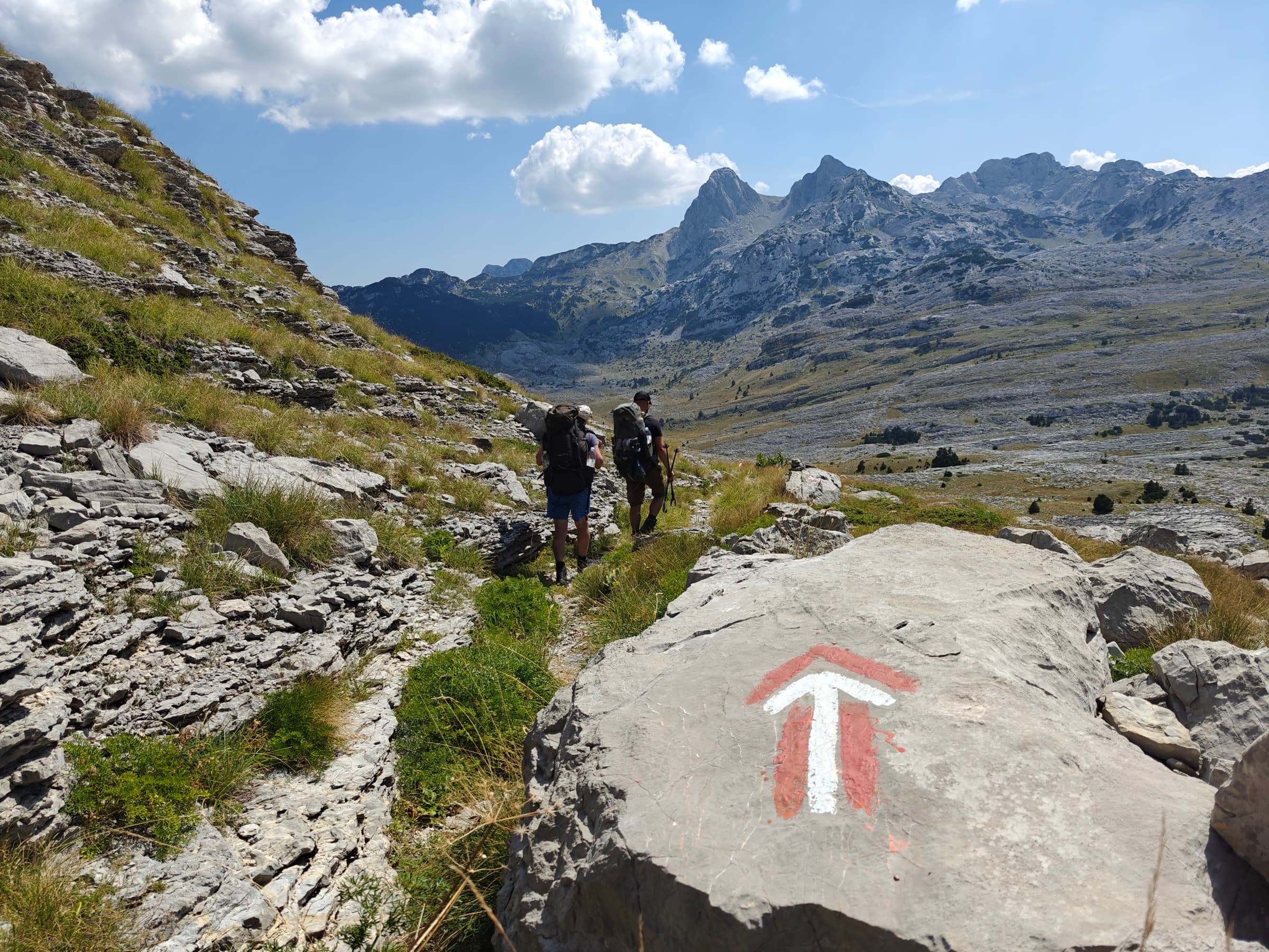 Two hikers walking past a red and white waymark painted on a boulder
