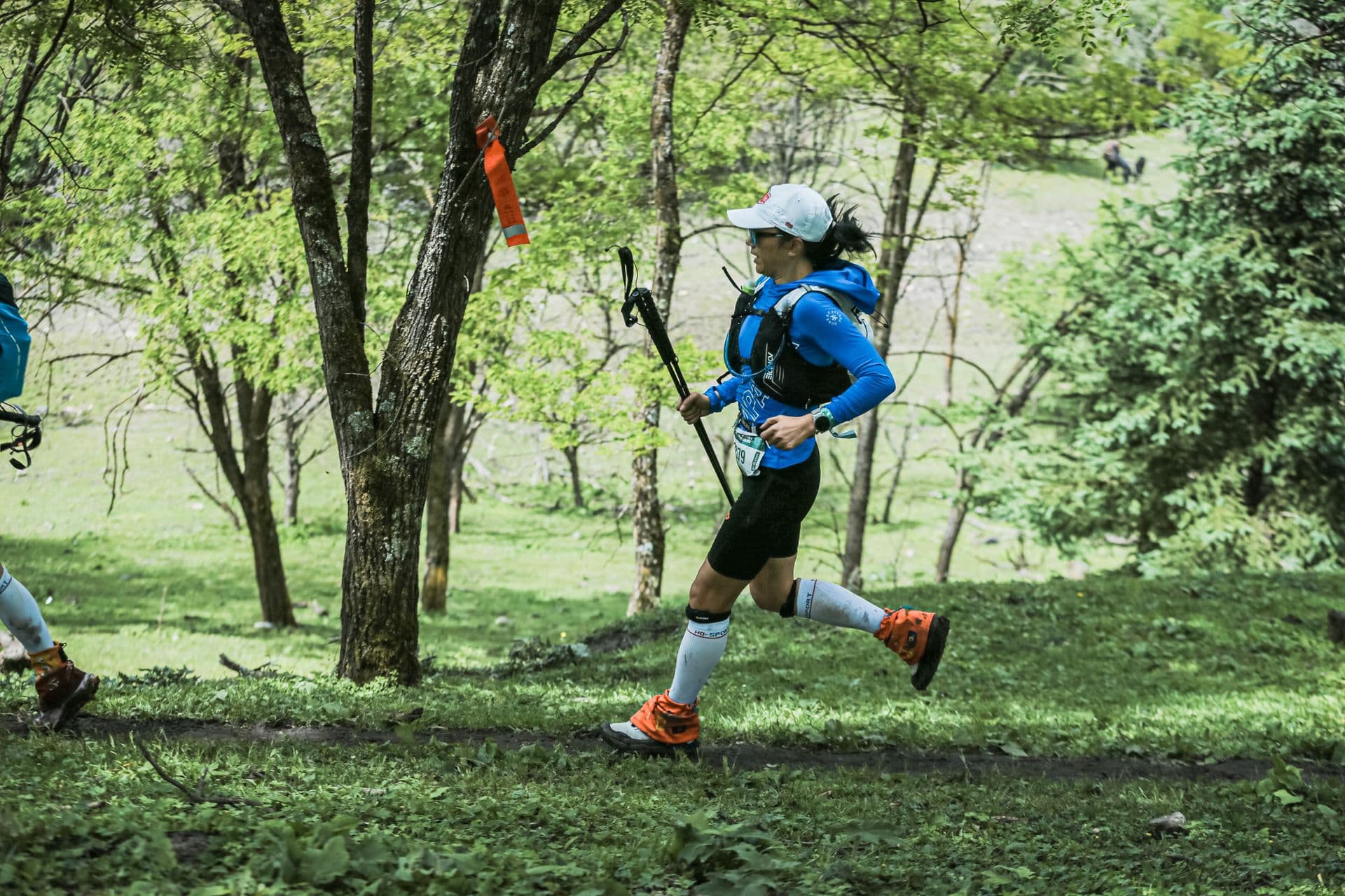 Trail runner with poles on a forest singletrack, the kind of terrain where Topo vs Hoka matters