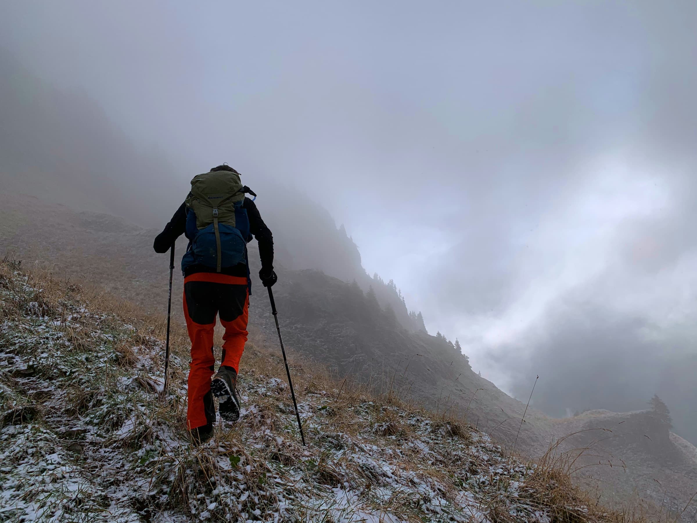 Hiker with trekking poles climbing a steep, frosty mountain slope in fog, the kind of terrain where hiking boots for bad knees matter